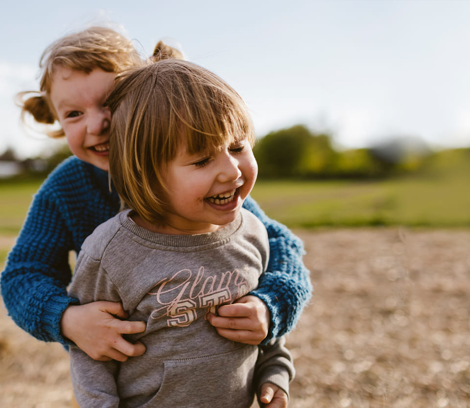 Close-up shot of two toddlers embracing while playing in an open field.
