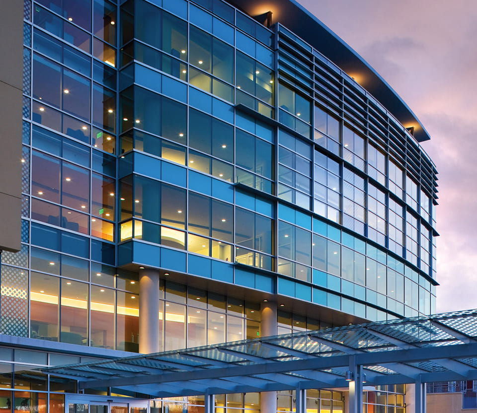 Angled view of a glass-front building with beautiful sunset lighting bouncing off the windows.