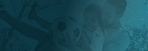 Blue-tinged photo of a father hugging his child that is holding a soccer ball.
